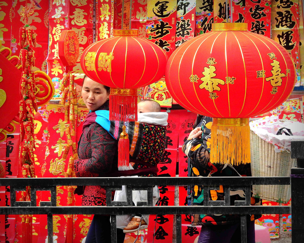 图:春节临近,年味渐浓.贵州一位妇女身背小孩在逛年货市场\中新社